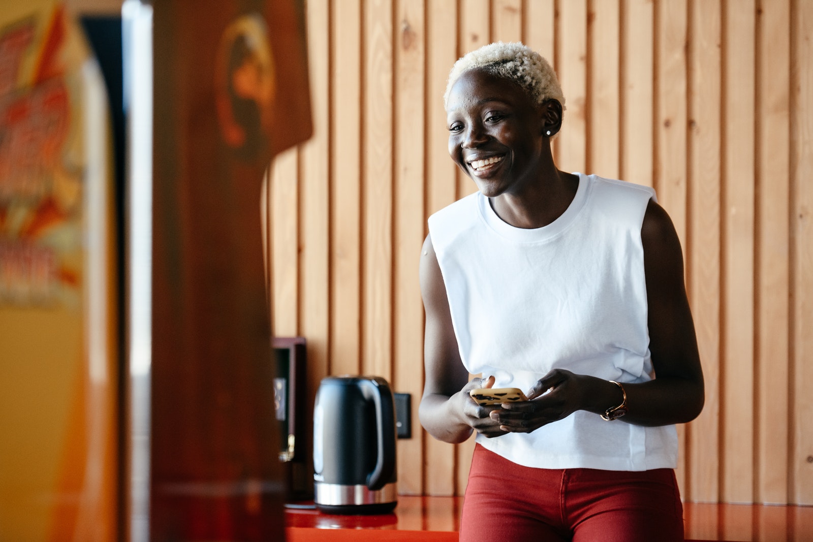 Young happy black woman using smartphone in office kitchen