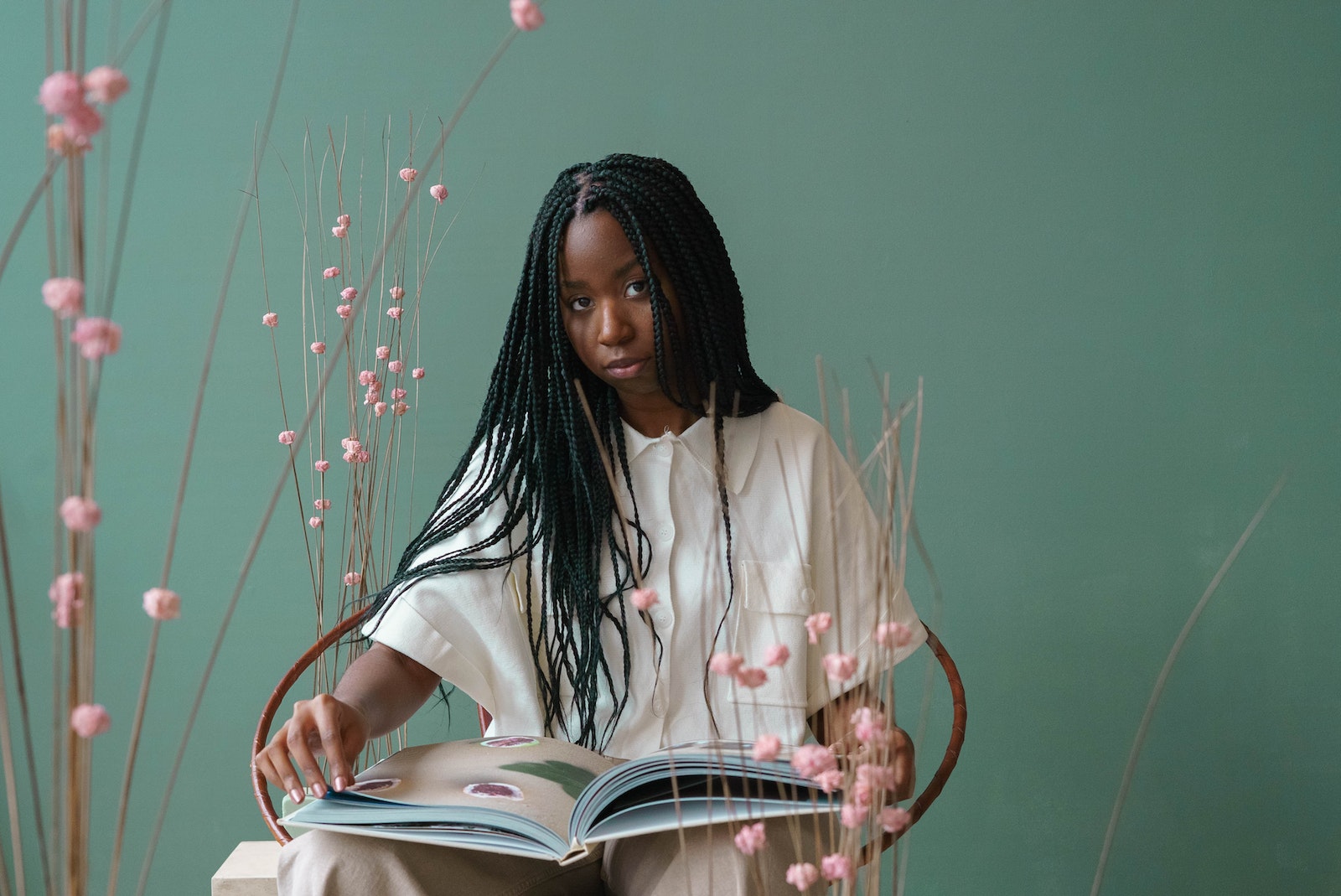Concentrated young black woman reading illustrated book in green studio near blooming flowers