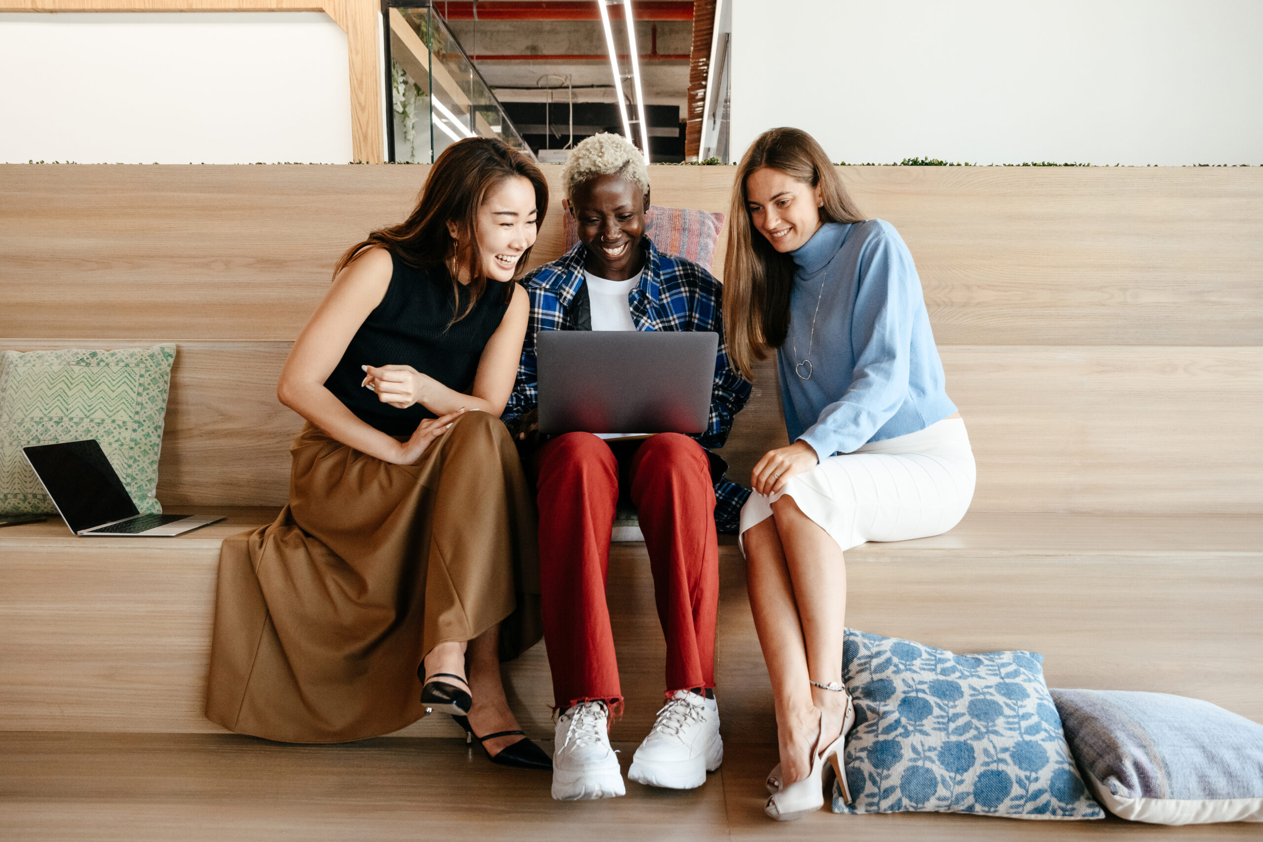 Young positive diverse women sharing laptop during work